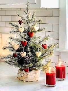 Small Christmas tree with red ornaments and lights next to red candles on white surface