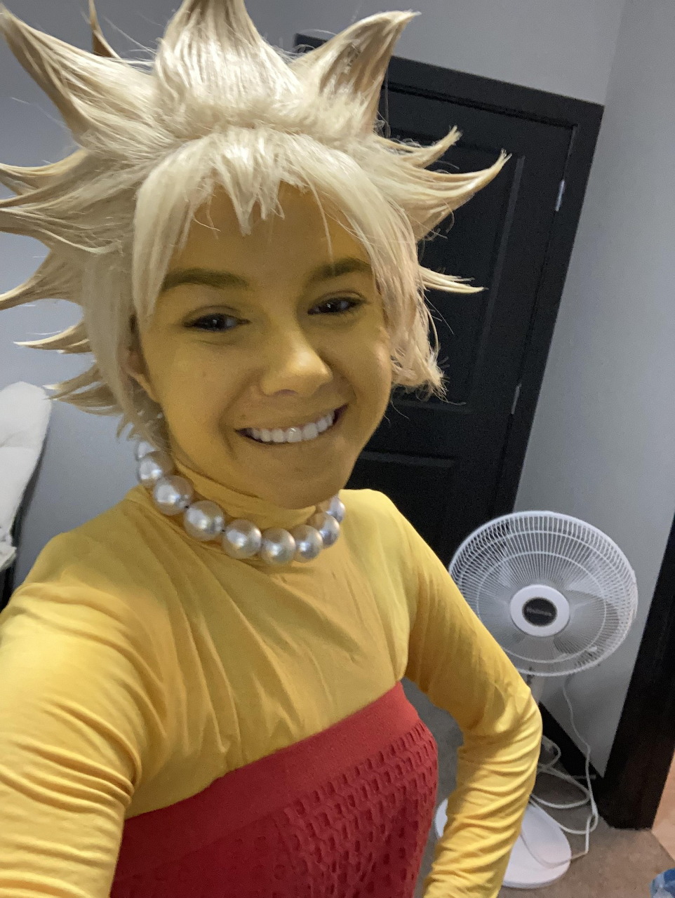 Person in spiky blonde wig and yellow shirt cosplay taking a selfie indoors