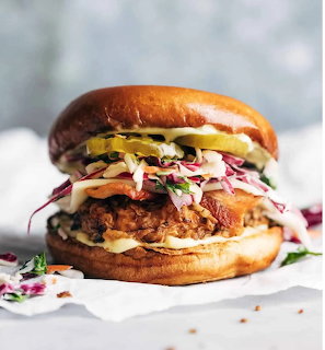 Close-up of a crispy fried chicken burger with colorful slaw and pickles on a golden bun