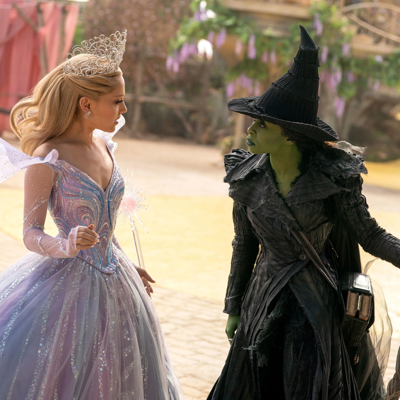 Glinda in pink dress and Elphaba in black witch costume from Wicked movie standing outdoors