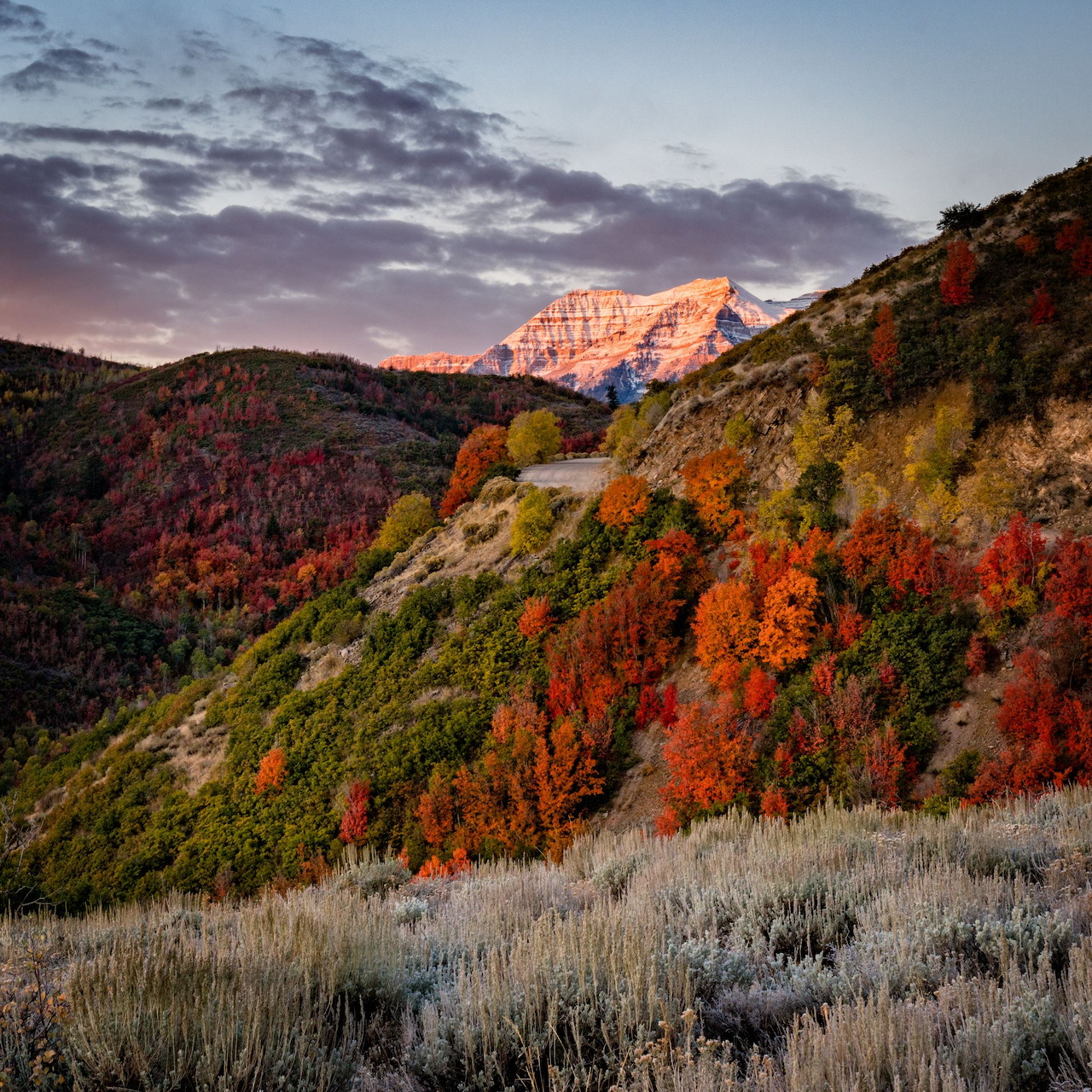 Sunlit mountain peak above colorful autumn hills and a grassy slope under a cloudy sky