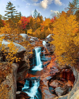 Cascading waterfall surrounded by colorful autumn trees with golden and red foliage on rocky terrain