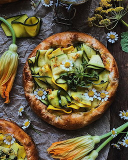 Pizza with zucchini ribbons, yellow squash blossoms and white flowers on rustic dark wood background