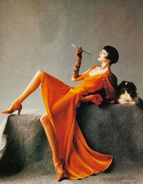 Elegant woman in orange vintage gown reclining with a small dog, holding a cigarette