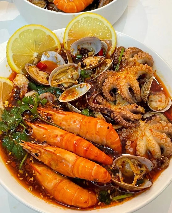 Bowl of mixed seafood with prawns, clams, octopus and lemon garnish in rich broth