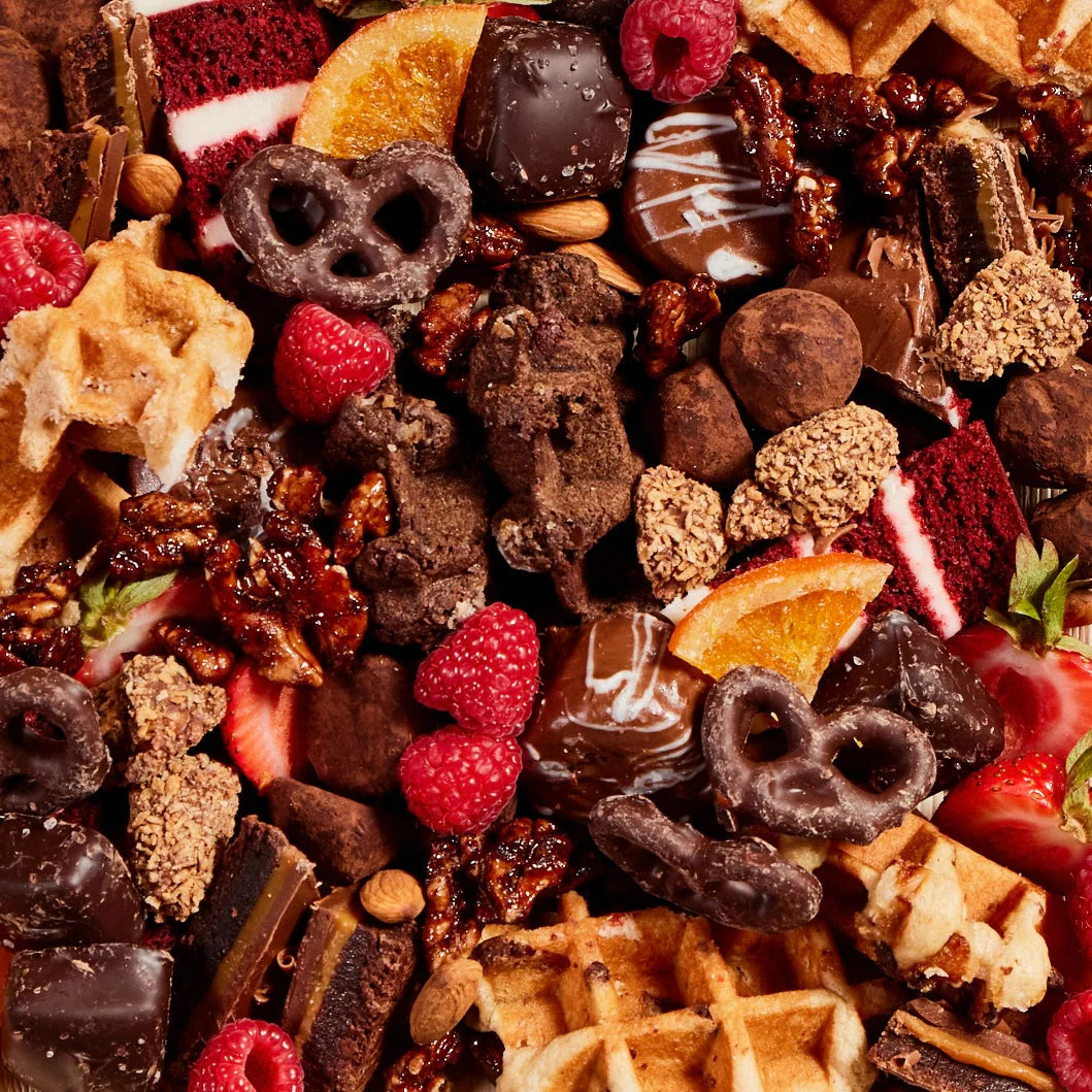 Close-up of a dessert board with chocolate sweets, waffles, berries, and orange slices
