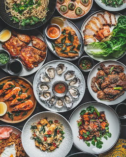 Overhead flatlay of seafood dishes including oysters, grilled fish, shrimp, mussels, and fresh salads on white plates