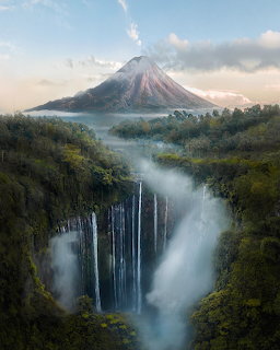 Aerial view of Tumpak Sewu waterfall with Mount Semeru volcano rising above misty jungle in Indonesia