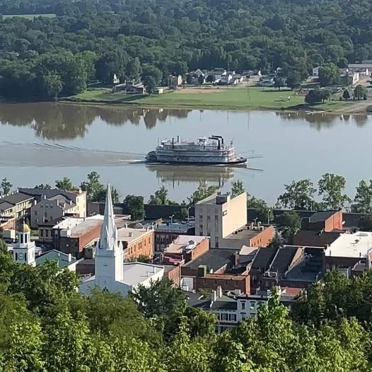 Elevated view of a town with a church steeple and a riverboat on a wide river