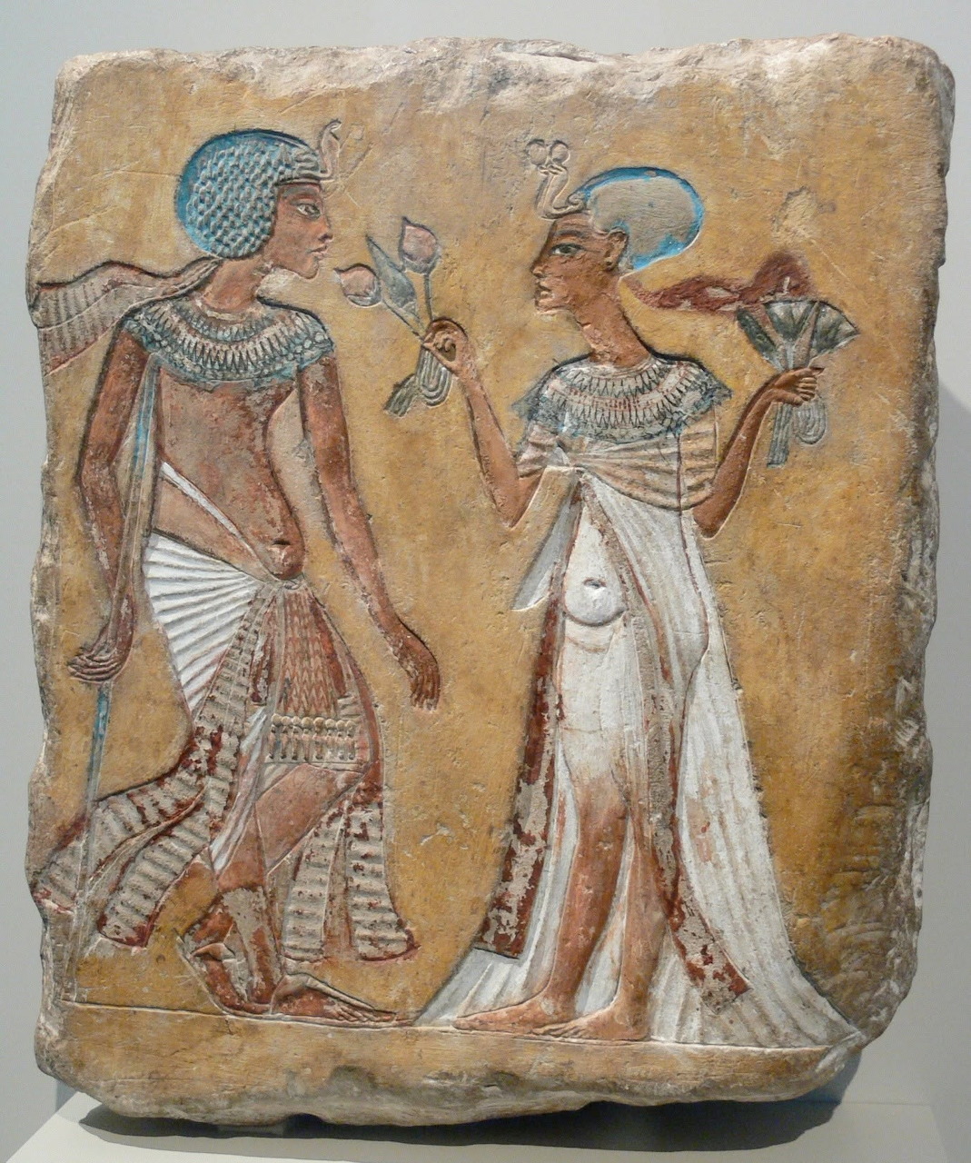 Ancient Egyptian relief of two figures exchanging a flower against a weathered ochre background.