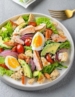 Overhead view of a chicken salad bowl with boiled eggs, avocado, tomatoes, red onion, and croutons