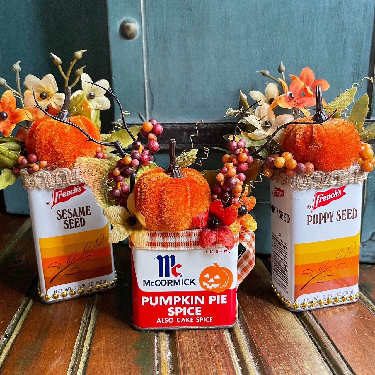 Fall decorations with orange pumpkins, flowers, and spice containers on wooden surface