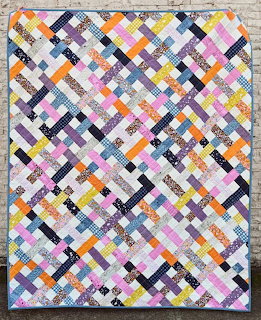 Colorful patchwork quilt with diagonal strips in pink, orange, yellow, gray, and black fabrics
