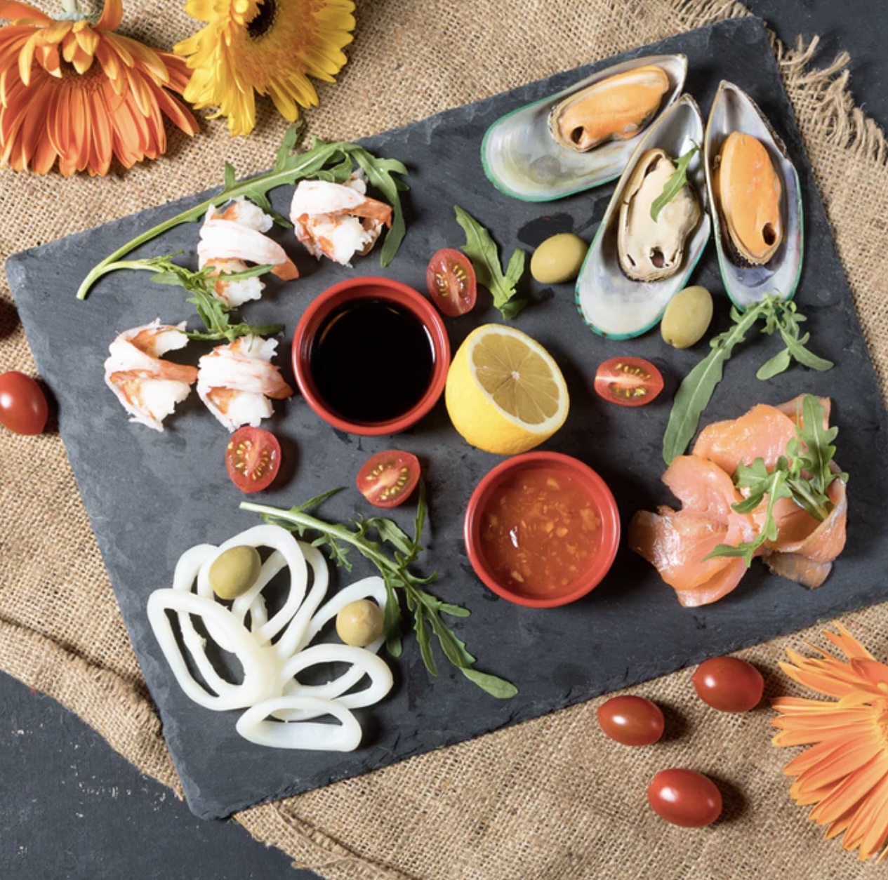 Seafood platter with salmon, mussels, shrimp, lemon, tomatoes and sauces on dark slate board