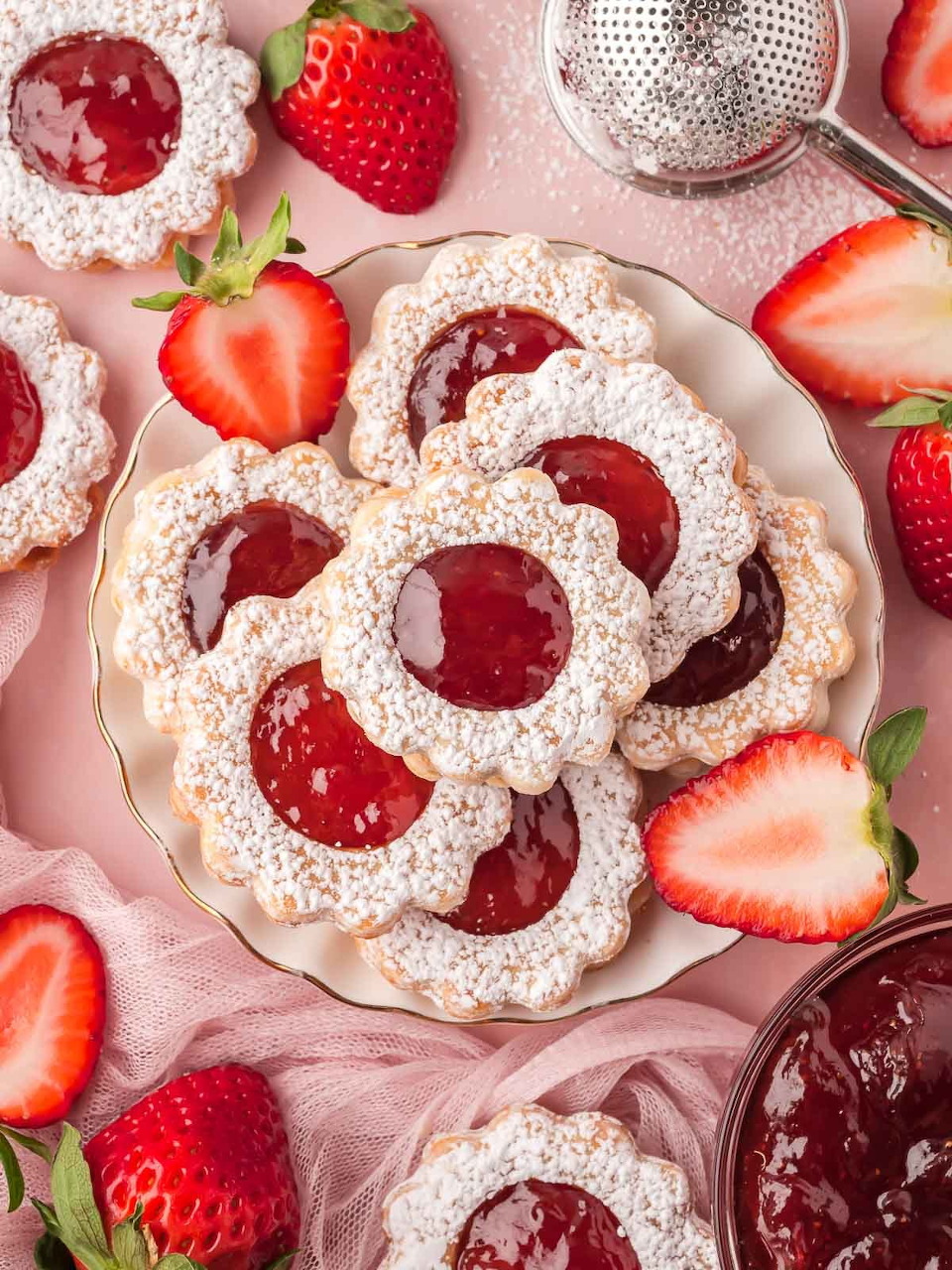 Powdered sugar jam cookies on a plate with fresh strawberries on a pink background