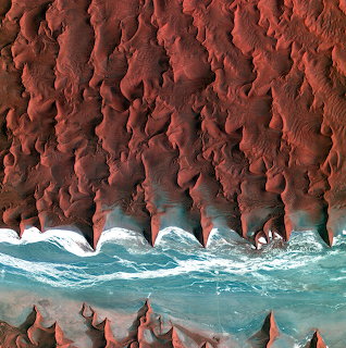Aerial view of turquoise waves along steep red cliffs and rocky shoreline