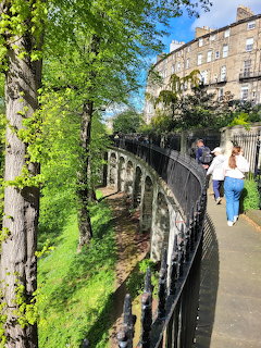 Curved walkway beside stone arches, green trees, and an old building in Moray Gardens