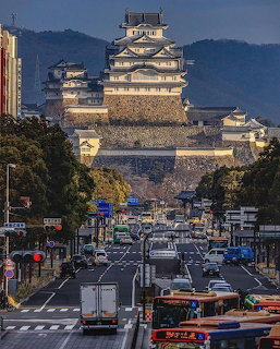 Himeji Castle above a busy street with cars, buses, and buildings