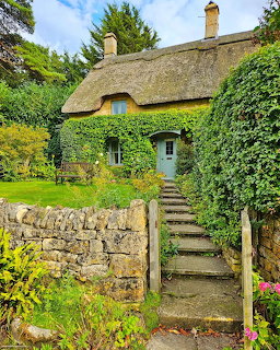 Stone cottage with thatched roof, ivy walls, blue door, and garden steps in the Cotswolds