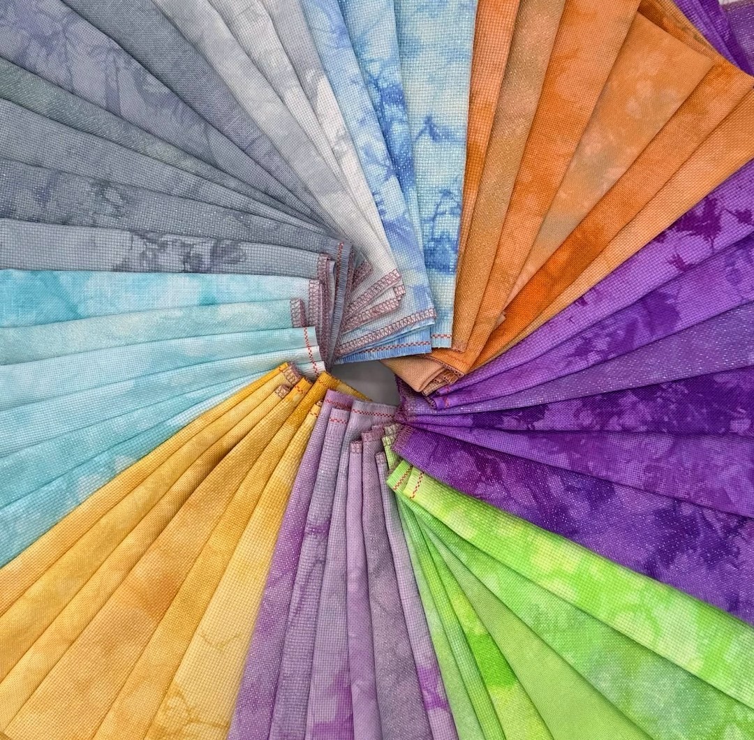 Hand dyed cross stitch fabric pieces arranged in a rainbow fan pattern