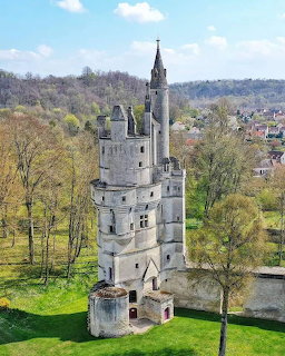 Tall medieval stone tower of Septmonts Castle with surrounding trees and village buildings