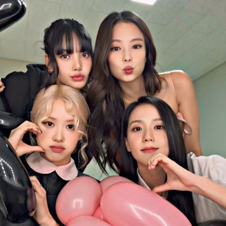 Four young women posing together indoors with hand hearts and pink balloons