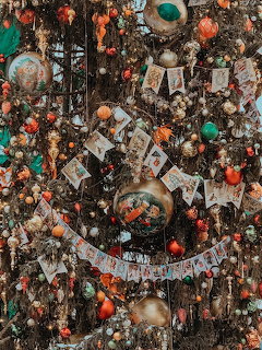 Christmas tree covered in vintage ornaments, colorful baubles, beads, cards, and decorative items in a dense arrangement