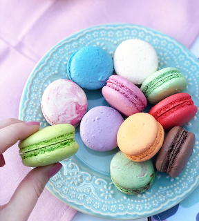 Hand holding a turquoise plate of colorful French macarons arranged in a circle