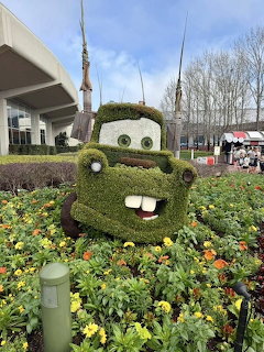 Green topiary sculpture of Tow Mater tow truck character surrounded by flowers at Disney theme park