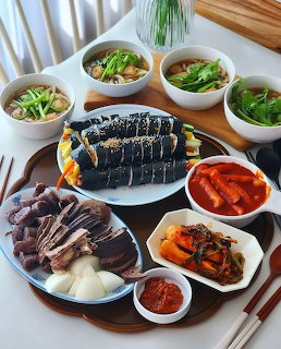 Korean food spread with kimbap, tteokbokki, sliced meat, kimchi, and side dishes on a table