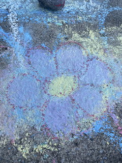 Colorful chalk drawing of a purple flower with yellow center on gray pavement