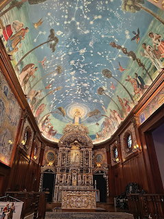 Ornate church interior with painted blue ceiling, altar, and dark wood paneling