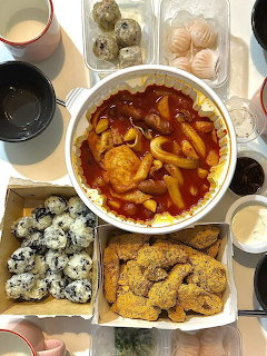 Top-down Korean food spread with tteokbokki, fried chicken, rice balls, dumplings, and sauces