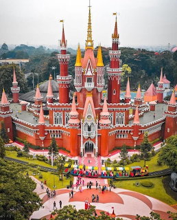 Ornate red and white castle with colorful towers and spires in landscaped grounds