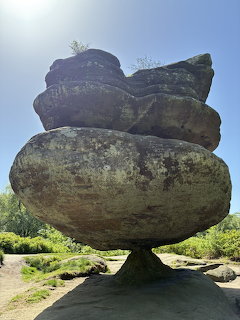 Large balancing rock formation of stacked boulders on a thin pedestal surrounded by greenery at Brimham Rocks
