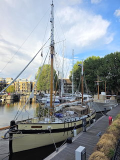 Historic sailing boat mored at a marina with masts, dock, buildings and trees in the background