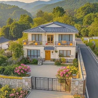 Two-story white villa with balconies and pink flower gardens surrounded by green mountains