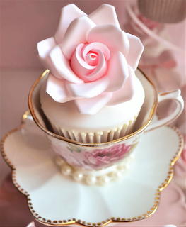 Cupcake with pink fondant rose in vintage teacup and saucer on decorative plate with pearl beads