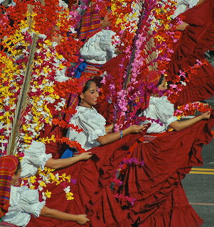 Women in red skirts and white tops dancing in a parade with colorful flower decorations