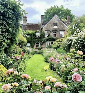 Traditional English stone cottage surrounded by vibrant rose garden and green lawn