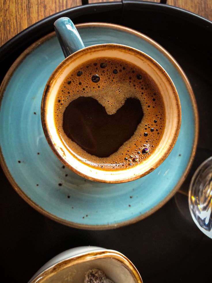 Coffee cup with heart-shaped foam on turquoise saucer viewed from above