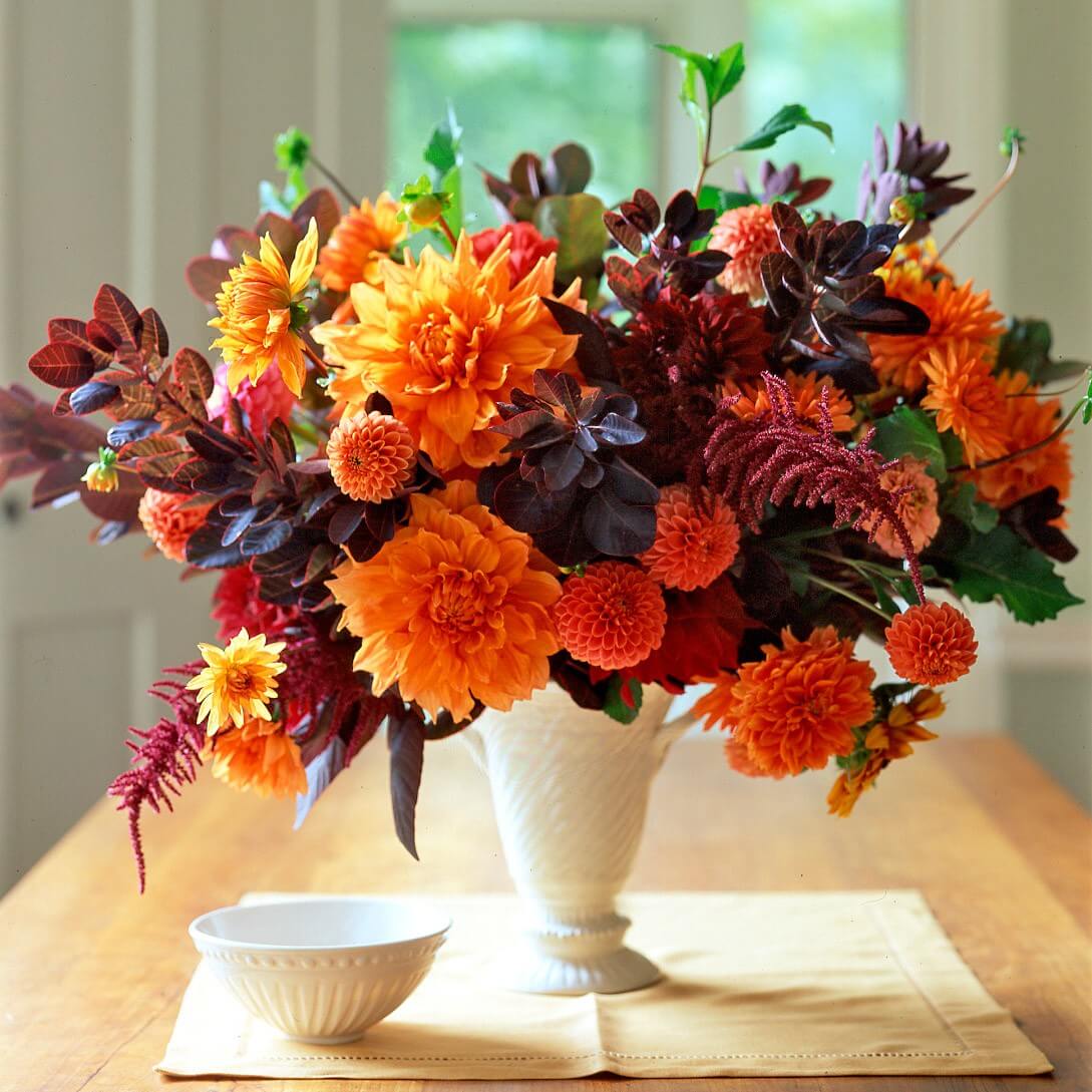 Colorful autumn flower bouquet in white vase with orange and burgundy flowers