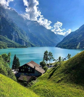 Traditional Swiss chalet on hillside overlooking turquoise alpine lake with mountains and cloudy sky