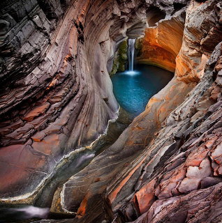 Waterfall flowing into blue pool surrounded by curved orange and gray canyon walls