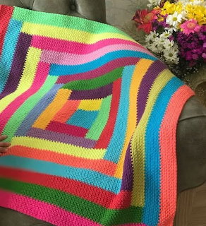 Colorful rainbow striped crochet blanket with geometric rectangular pattern on gray couch