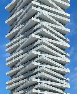 Close-up of a modern high-rise tower with stacked white balconies against blue sky
