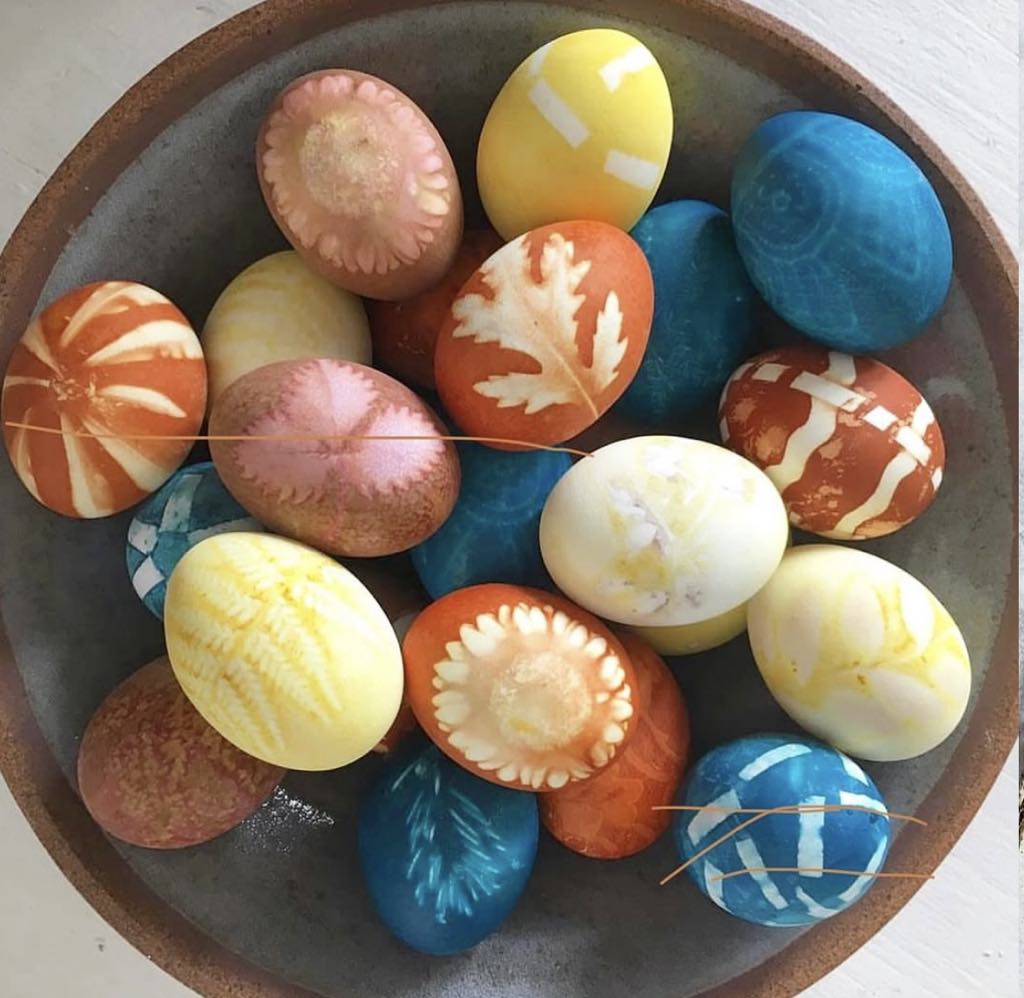Colorful decorated Easter eggs with leaf and floral patterns arranged in a round ceramic bowl