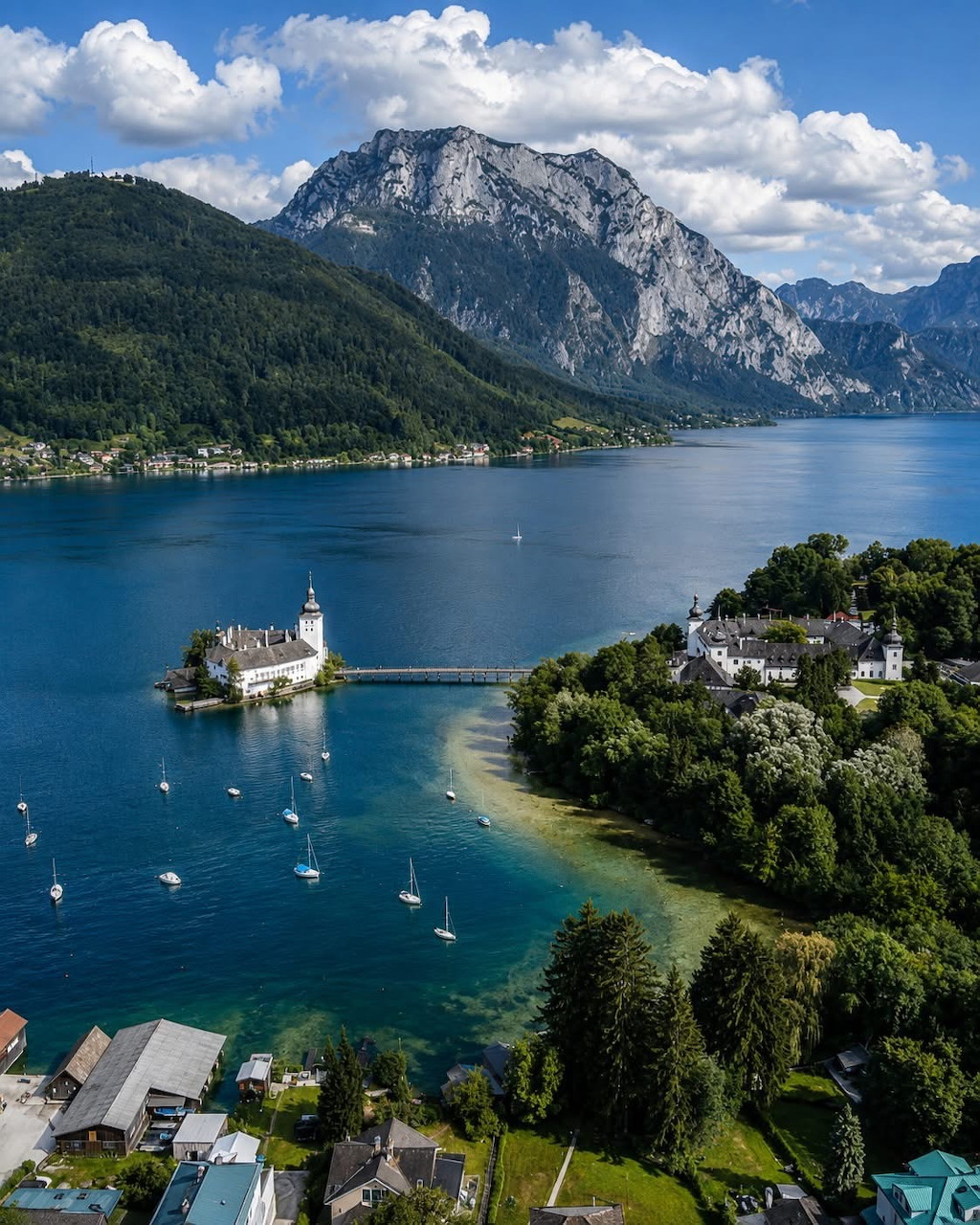 Island castle on a blue lake with sailboats and mountains behind