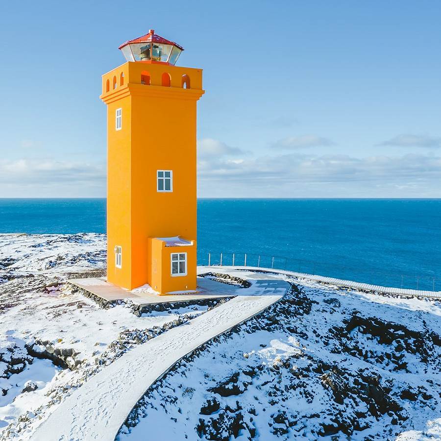 Orange lighthouse on snowy Icelandic coast with blue ocean