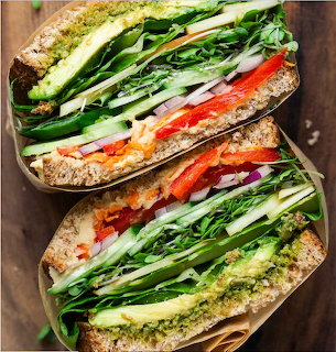 Two halves of a vegetable sandwich with avocado, cucumber, greens, and red pepper on whole grain bread
